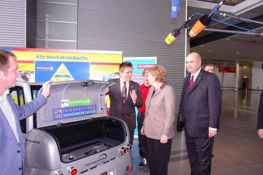 Wilhelm Hülsdonk (m.) erläutert der Bundeskanzlerin im Beisein von ZDH-Präsident Otto Kentzler (r.) die Maßnahmen des Kfz-Gewerbes zur E-Mobilität.