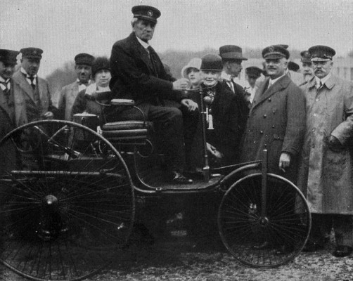 Carl Benz thront auf seiner Erfindung