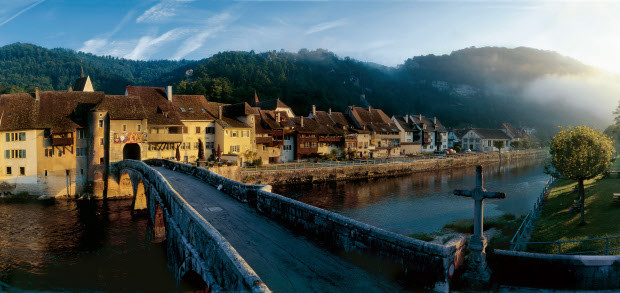 Mit der spaetromanischen Stiftskirche, den schmucken Haeusern und der alten Steinbruecke gilt St-Ursanne am Doubs als 'Perle des Jura'.